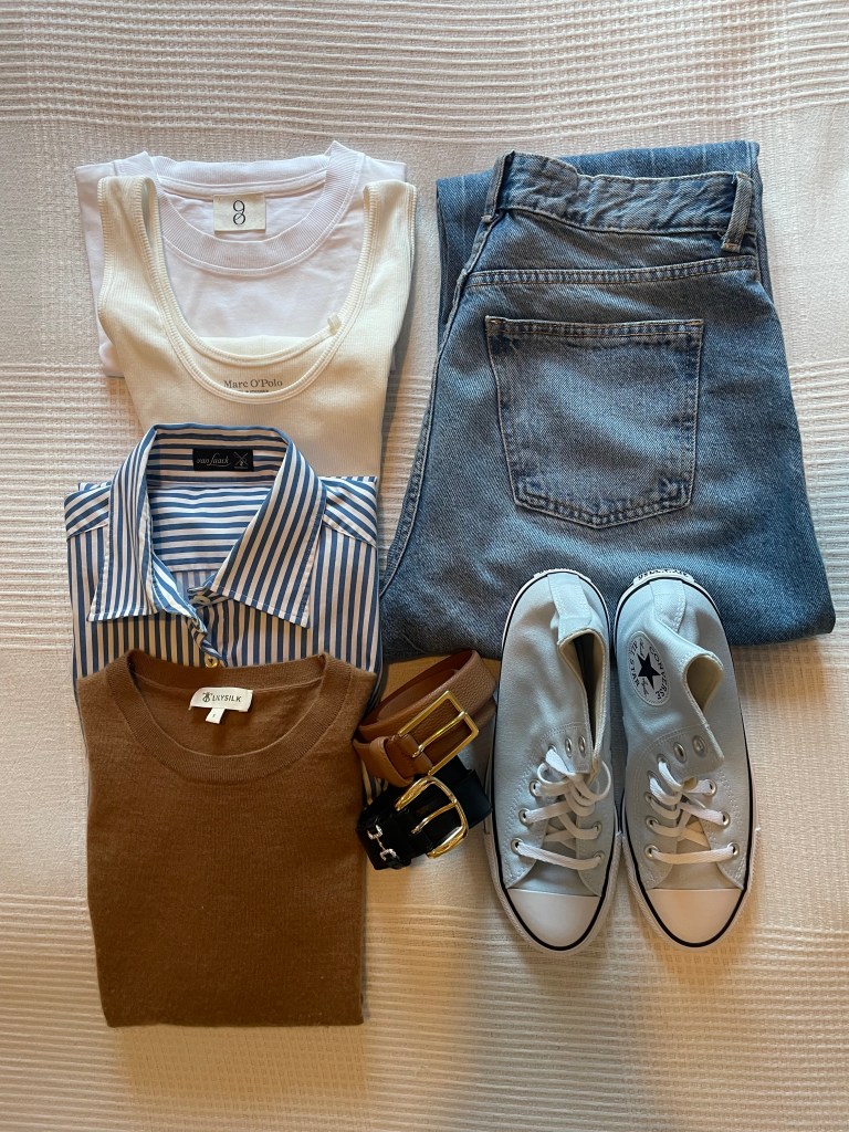 Basic staple outfit with a striped shirt, white t-shirt and jeans laid out on the bed.