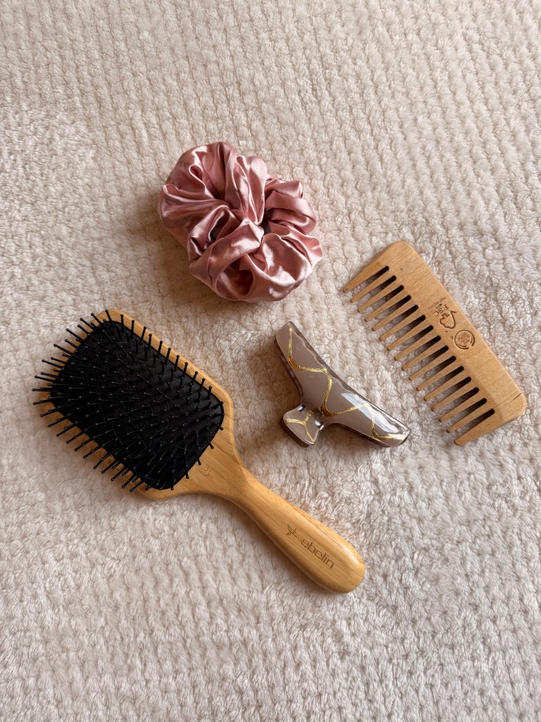 Hair brush and hair essentials in rosy and natural colours spread out aesthetically.