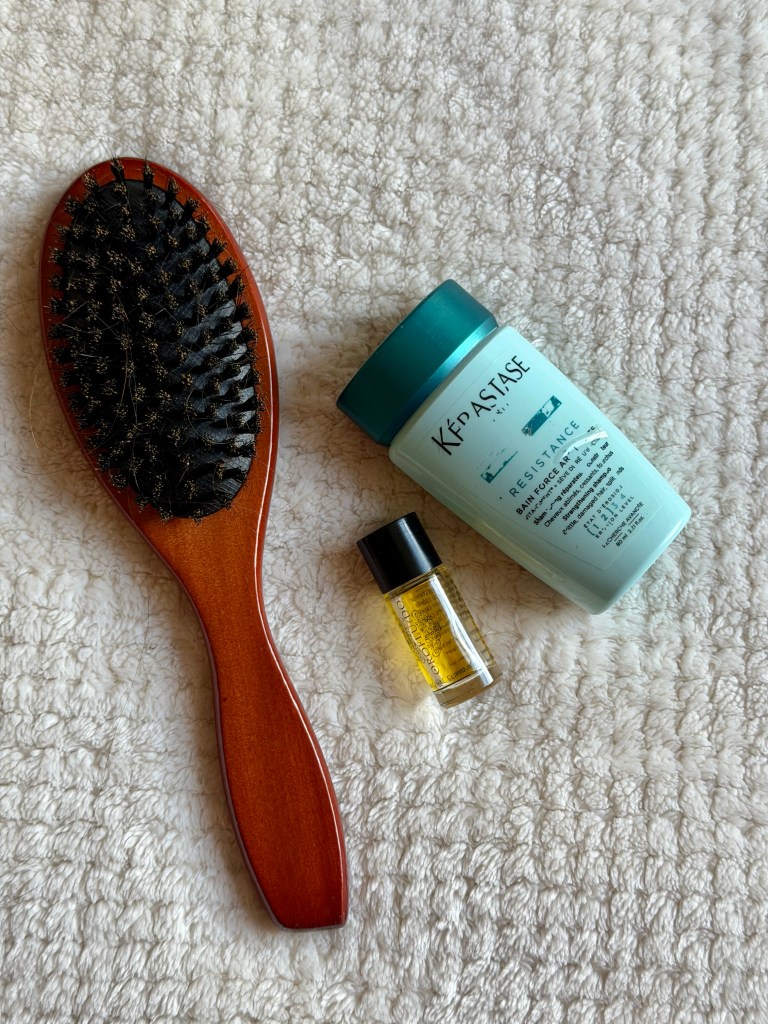 A hair brush placed beside to miniature hair products